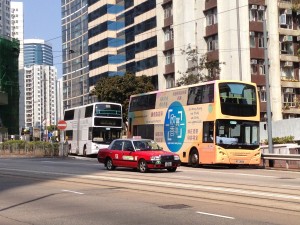 ２階建てバスと赤いタクシー、トラムが行き交う大通り。